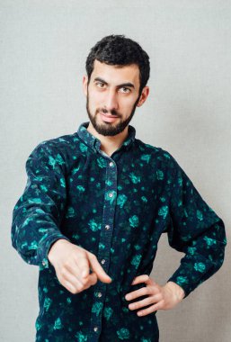 Mavi gömlekli yakışıklı beyaz adam gülümsüyor ve parmağıyla işaret ediyor.