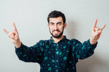 Çekici, sakallı ve gömlekli yetişkin bir adam izole edilmiş beyaz bir arka planda rock 'n roll' un el hareketlerini gösteriyor.