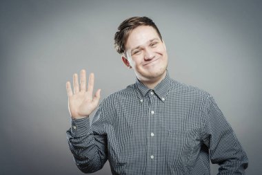 Genç adam el sallıyor, gülümsüyor.