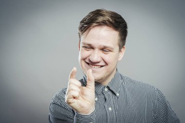 Genç ve yakışıklı bir adam. Jest yap. Gri bir arkaplanda