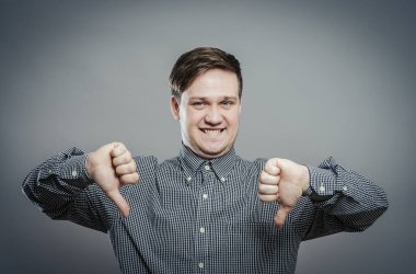 Yakışıklı genç adam başparmağını aşağı indirerek yumruğunu indirdi. Kapalı portre. Hoşnutsuz bir jest.