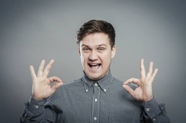 Tamam işareti işaretleniyor. Gömlekli ve kravatlı neşeli genç adam. Gri arka planda dururken işaret veriyor.