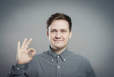 Tamam işareti işaretleniyor. Gömlekli ve kravatlı neşeli genç adam. Gri arka planda dururken işaret veriyor.