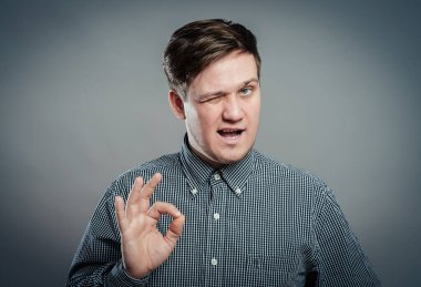 Tamam işareti işaretleniyor. Gömlekli ve kravatlı neşeli genç adam. Gri arka planda dururken işaret veriyor.