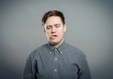 Yakından çekilmiş bir portre, komik, sinirli, kaba, kaba bir genç adam kamerana dilini uzatıyor, izole edilmiş gri bir arka plan. Olumsuz duygu yüz ifadesi duygular, işaretler, semboller