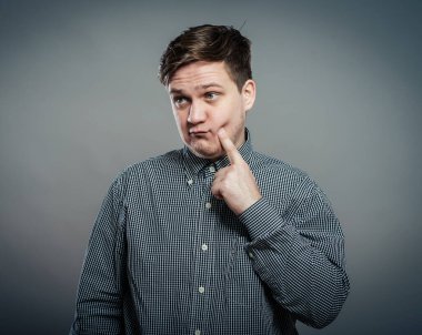 Öp beni! Şaşırmış genç adam, gri arka planda dururken dudaklarını gösterip gülümsüyor.