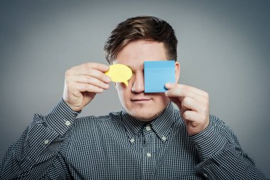 Gri arka planda gözlerini kapayan bir kağıt parçasıyla genç bir adamın yakın plan portresi.