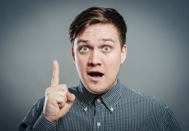 Gri arka planda dikilirken yukarı bakan gülümseyen genç adamın portresi. Dikey çekim.