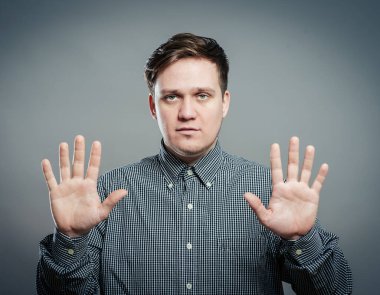 Gri arka planda gülümseyen elleri havada yakışıklı bir adamın portresi.