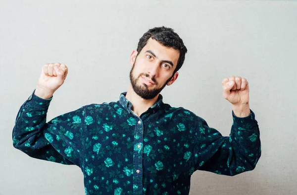 Zirveye ulaştım! Gri arka planda dururken gülümseyen mutlu genç adam.