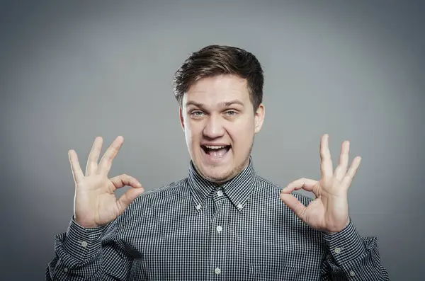 Tamam işareti işaretleniyor. Gömlekli ve kravatlı neşeli genç adam. Gri arka planda dururken işaret veriyor.