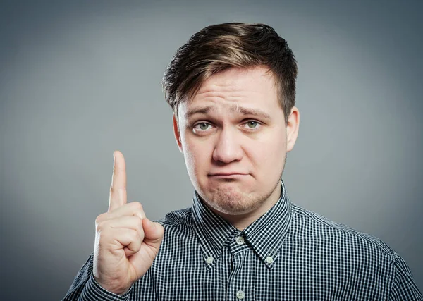 Portrait of disappointed young man pointing upwards while standing against gray background. Vertical shot.