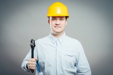 İngiliz anahtarı ve kolları katlanmış, kazan dairesinde gülümseyen genç bir tamirci. 