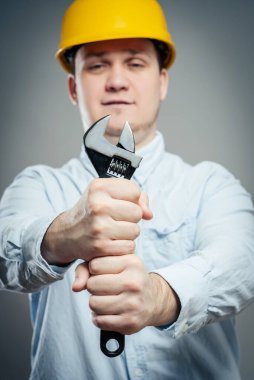 İngiliz anahtarı ve kolları katlanmış, kazan dairesinde gülümseyen genç bir tamirci. 