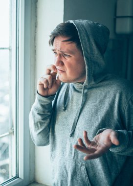 Kapüşonlu adam pencerede telefonla konuşuyor.