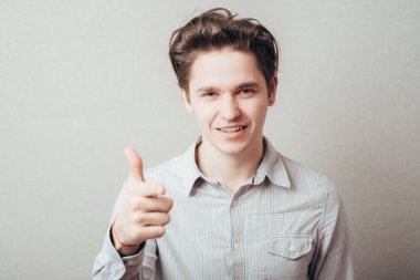 Gri bir arkaplan üzerinde parmağını gösteren genç bir adamın portresi.