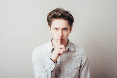 Stüdyo portresi genç bir adamın sessiz bir jest yapması, gri arka plan.