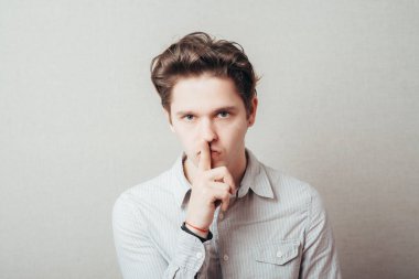 Stüdyo portresi genç bir adamın sessiz bir jest yapması, gri arka plan.