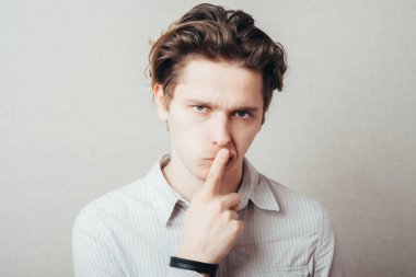 Stüdyo portresi genç bir adamın sessiz bir jest yapması, gri arka plan.