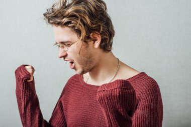 Gözlüklü adam zaferin sevincini haykırıyor. Gri bir arkaplanda.