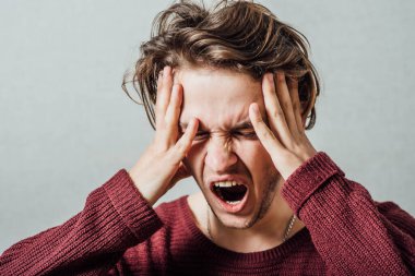 Adam ellerini başının üstüne koyup bağırıyor. Gri bir arkaplanda.