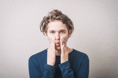 Genç adam elleriyle yanaklarını sıkıyor.