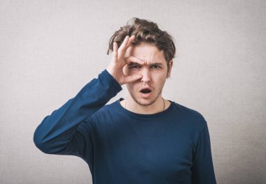 Genç adam ellerini gözlükmüş gibi gözünün üstünde tutuyor ve parmaklarından bakıyor.