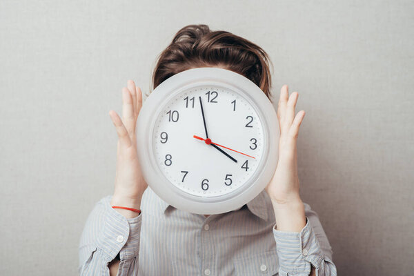 Portrait Of A Young Man Holding A Clock On Gray Background