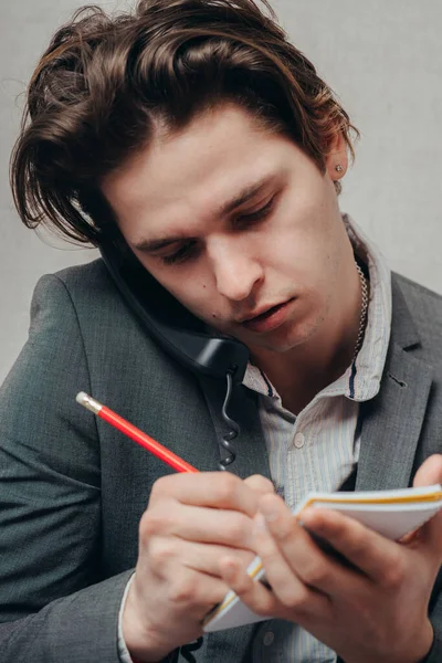 Concentrated on work. Confident young man talking on the landline telephone and writing something in note