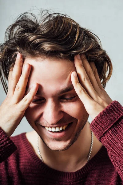 Man hands on head laughing. On a gray background.