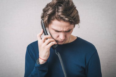 Ofisi ya da ev telefonu olan genç bir adam. Gri bir arkaplanda.