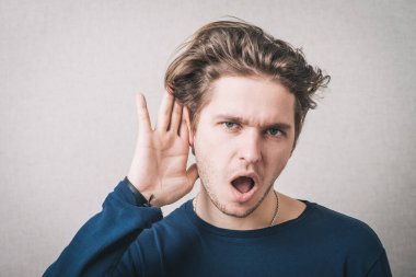 Eli kulağının dibinde dinleyen bir adam. Gri bir arkaplanda.