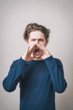 Bir adam elleri ağzının yanındayken bağırır. Gri bir arkaplanda.