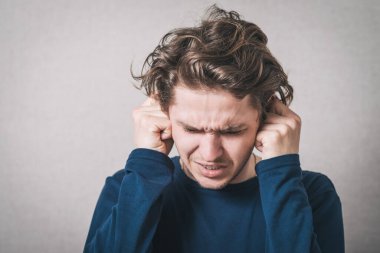 Adam elleriyle kulaklarını kapattı. Gri arkaplan.