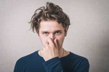 Adam eliyle burnunu kapattı. Gri arkaplan.