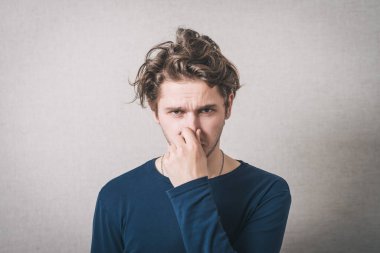 Adam eliyle burnunu kapattı. Gri arkaplan.