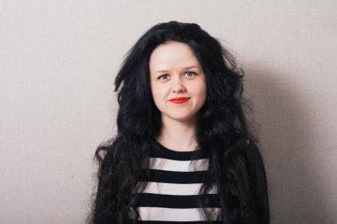 Uzun saçlı bir kadın kameraya bakıyor. Gri arkaplan