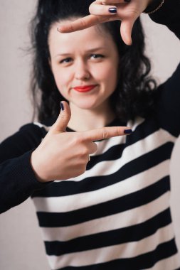 Parmak çerçevesinden bakan bir kadın. Gri arkaplan.