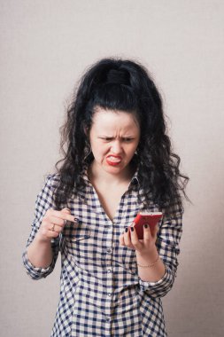 Telefonda hüzünlü mesajlar okuyan bir kadın. Gri bir arkaplanda.