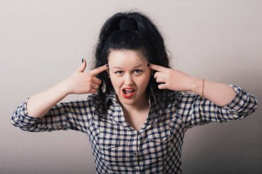 Esmer kız gri arka planda parmağını şakağına dayıyor.