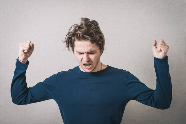 Man angry, shouts, lifting his hands up into fists. Gray background