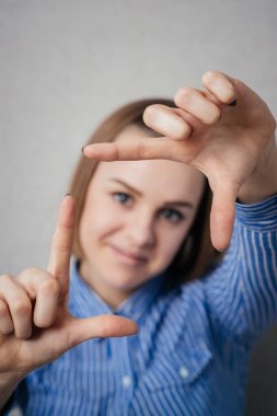 El hareketli parmak çerçevesi. Güzel genç bir kadın gri arka planda dururken kameraya ve işaret parmağına bakıyor.