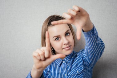 El hareketli parmak çerçevesi. Güzel genç bir kadın gri arka planda dururken kameraya ve işaret parmağına bakıyor.