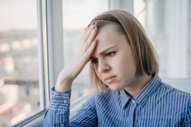 Depresyon ve stres yaşayan genç çekici bir kadın pencereye karşı acı ve keder içinde duruyor. Stüdyo ışıklarıyla kendini üzgün ve çaresiz hissediyor.