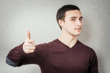 Gri bir arkaplan üzerinde parmağını gösteren genç bir adamın portresi.