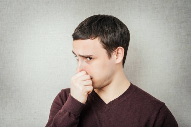 Genç iş adamı gri arkaplanı kapatıyor. Parmaklarıyla burnunu tutuyor.