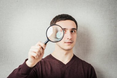 Gri arka planda büyüteç takan adam. - Normal bir adamın portresi..