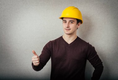 Sarı şapkalı inşaat işçisi. 20 'li yaşlarında mutlu bir erkek. Baş parmaklı genç adam portresi.