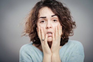 Genç, üzgün, üzgün, depresif, endişeli, iki eliyle başını tutmakta olan esmer kadının yakın plan portresi. İnsani duygular, yüz ifadeleri, duygular, algı