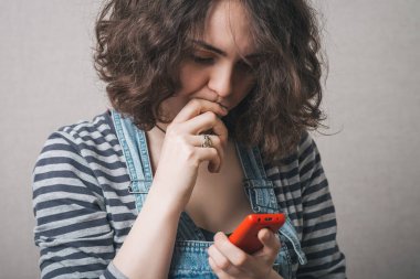 Telefondaki üzgün SMS mesajlarını okuyan bir kadın. Gri arkaplan